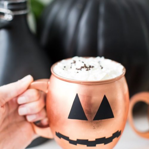 photo of a hand holding a copper mug with pumpkin face on it