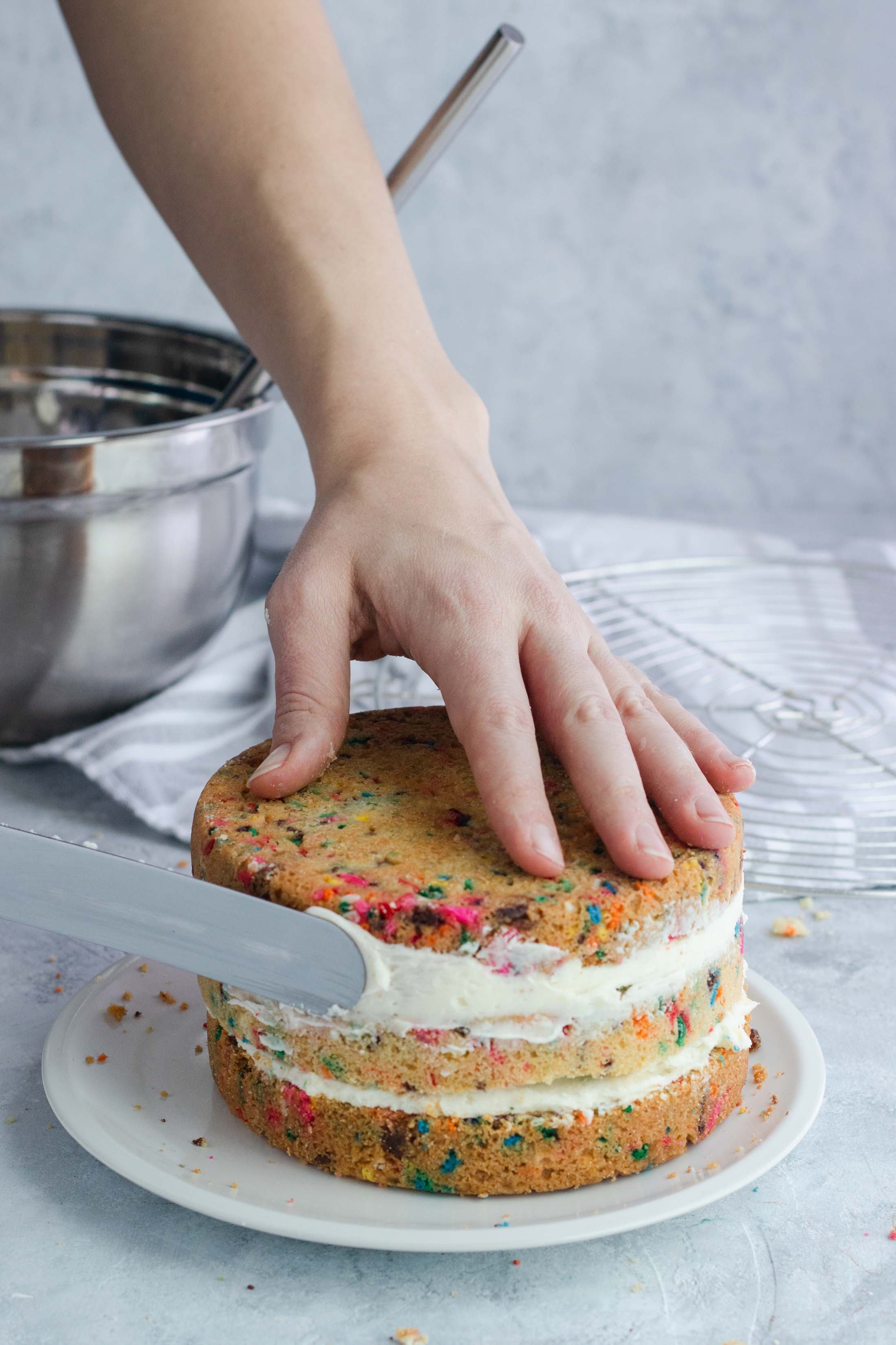 a photo of a funfetti Sugar Cookie Cake being frosted, recipe by top Houston lifestyle blogger Ashley Rose of Sugar & Cloth