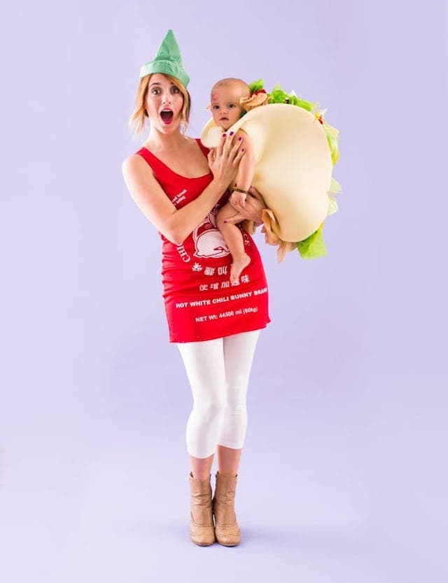 Photo of mother dressed as sriracha bottle costume holding baby dressed in taco costume