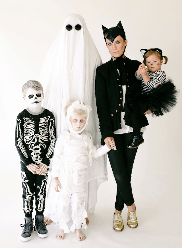 Photo of family in Halloween themed costumes: ghost, black cat, mummy, and skeleton