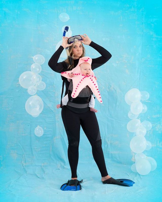 Photo of mother dressed in scuba gear carrying baby in star fish costume, in strap on baby carrier.