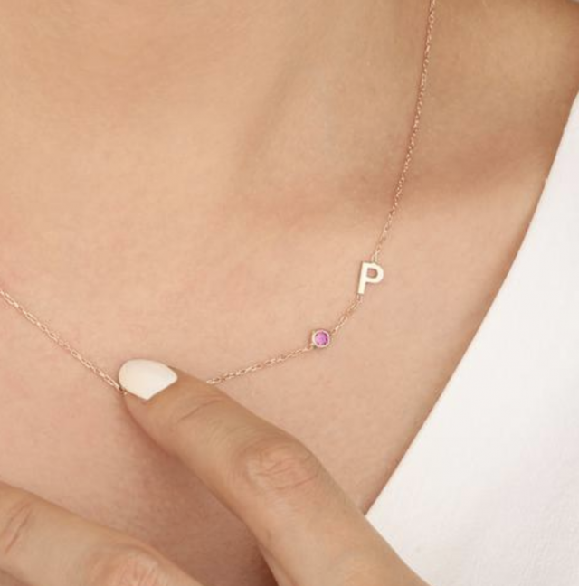 a womans hand touching a birthstone initial necklace gift