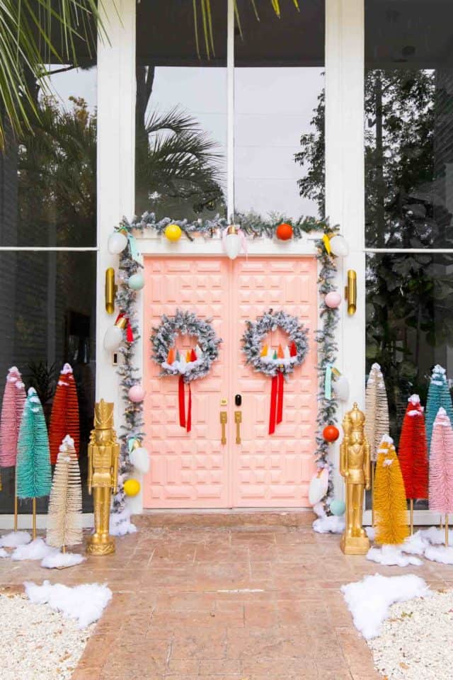 a pink door with front door christmas decor and giant bristle brush trees