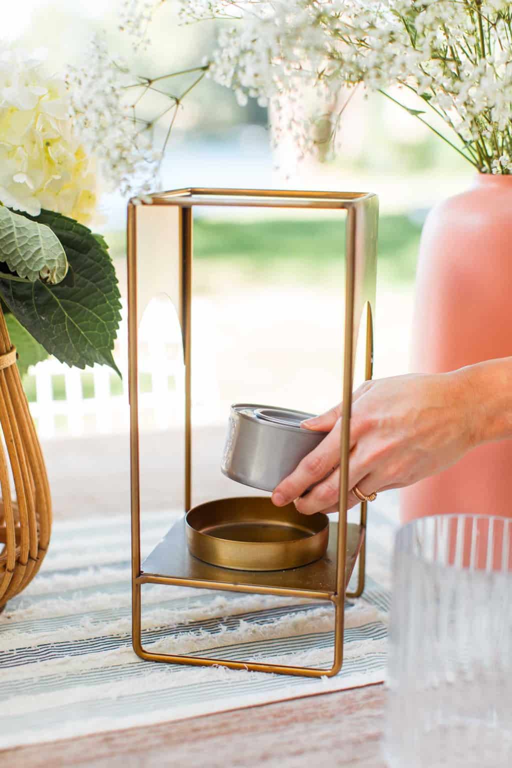 a hand placing a gel can on a gold lantern to show how to keep flies away outside