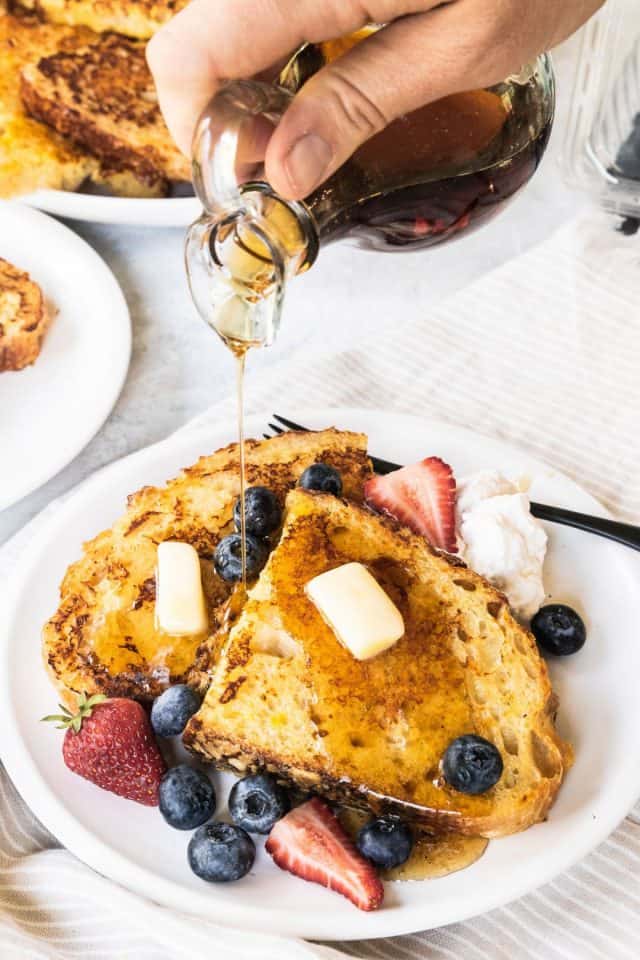 A serving of Sourdough French Toast with a topping of honey and butter surrounded with blueberries and strawberries 