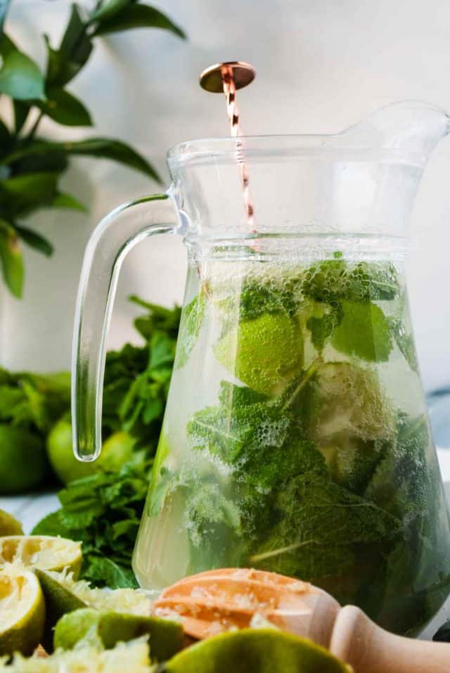 pitcher of mojitos - a pitcher of mojito drink surrounding freshly squeezed lime.