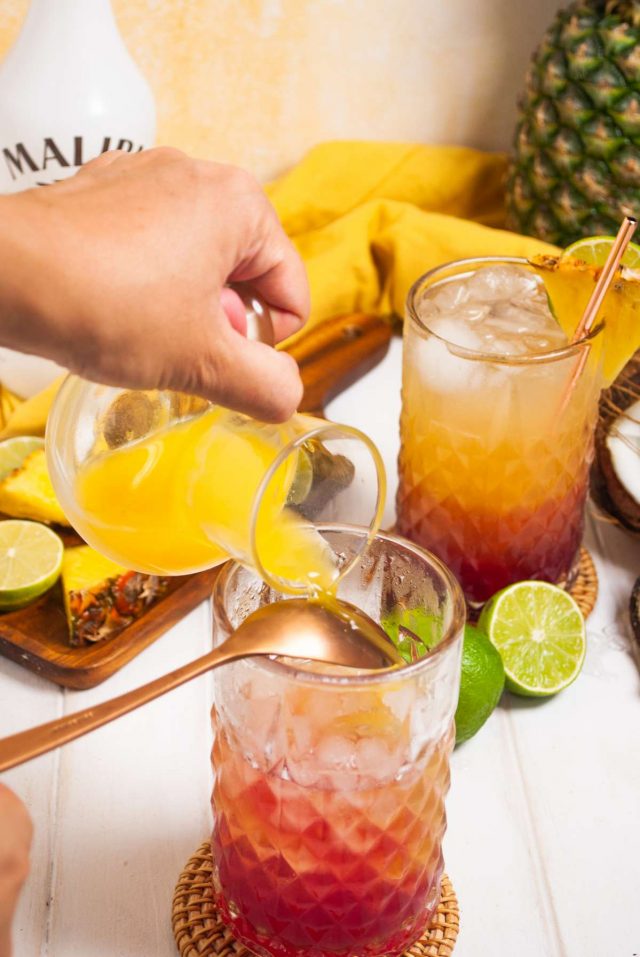 malibu bay breeze drink - pouring pineapple juice in a glass full of malibu rum