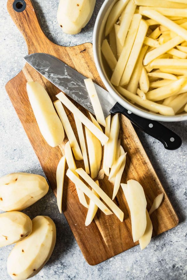 how to make french fries - chopped potatos in a cutting board and a knife