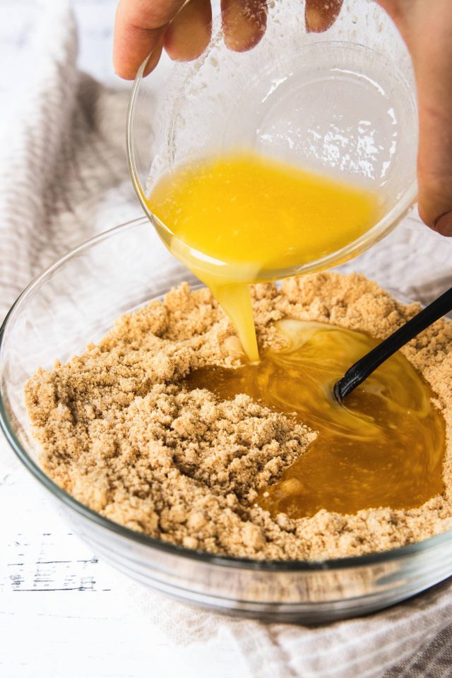 Pouring the melted butter into the graham cracker crumbs in a mixing bowl for the Caramilk Cheesecake recipe