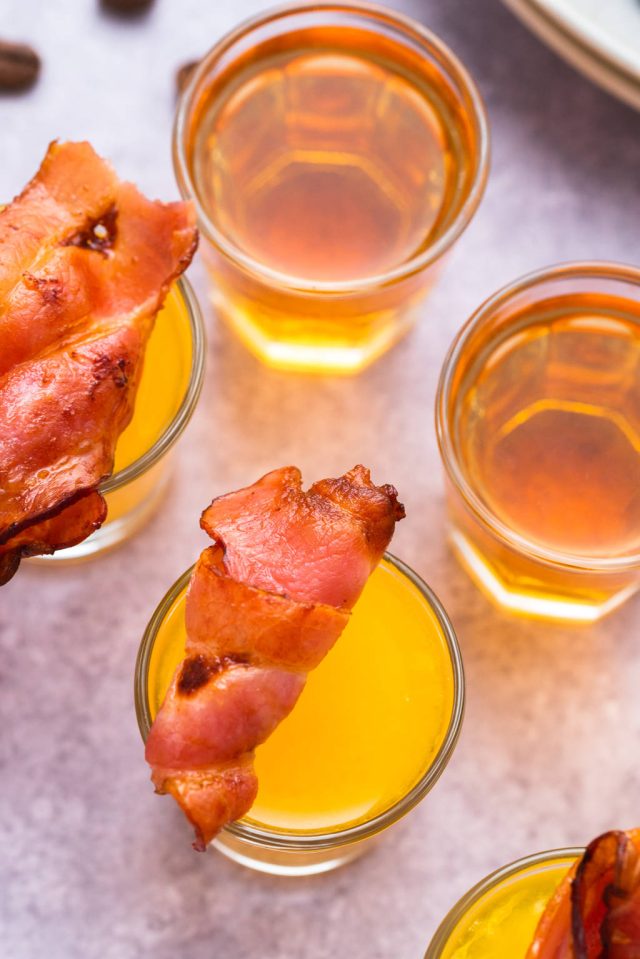 top view of a orange juice with bacon on top and shots on the side