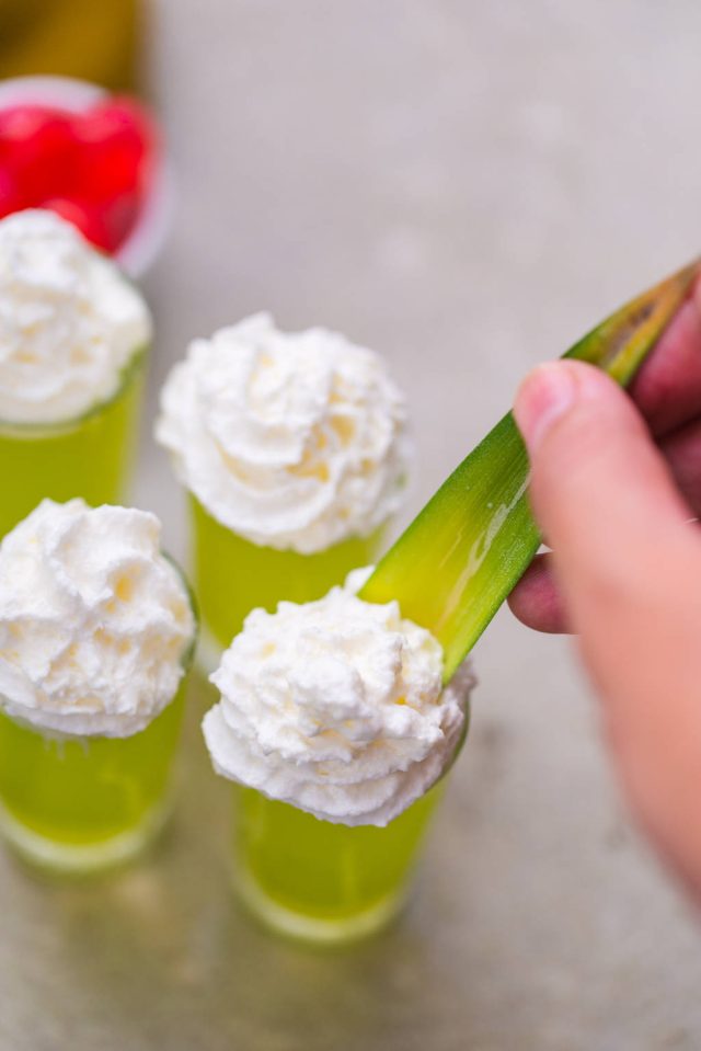 adding whipped cream, a pineapple leaf, and a cocktail cherry on top for garnish