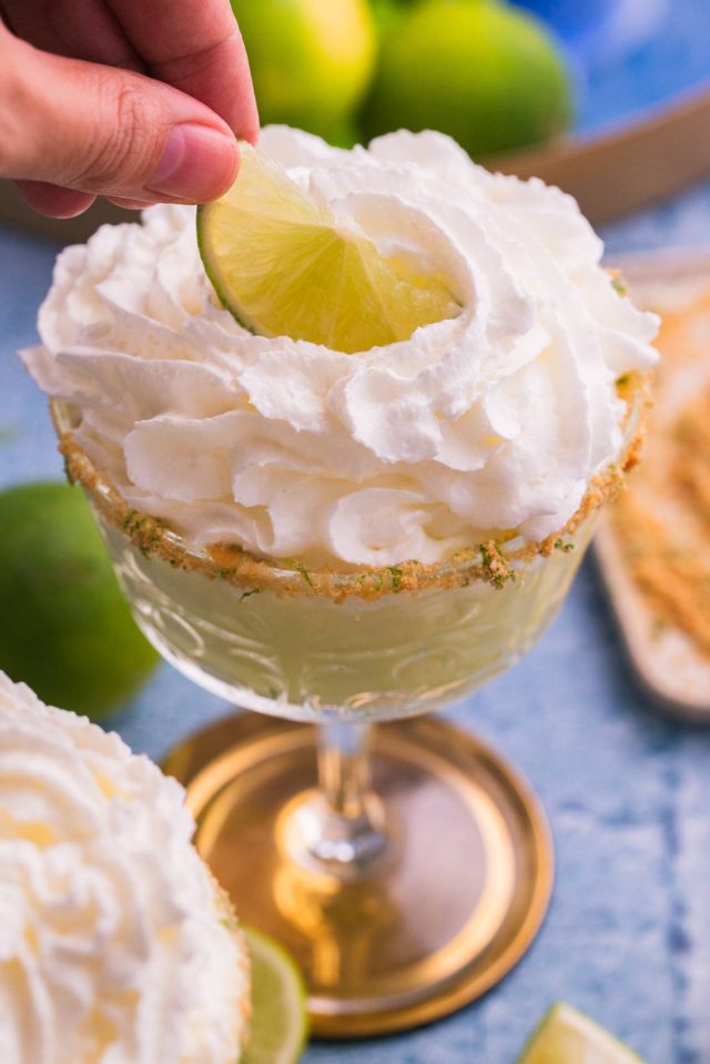 key lime martini with whipped cream, a sprinkle of the Graham crackers, lime zest, and a lime wedge as garnish